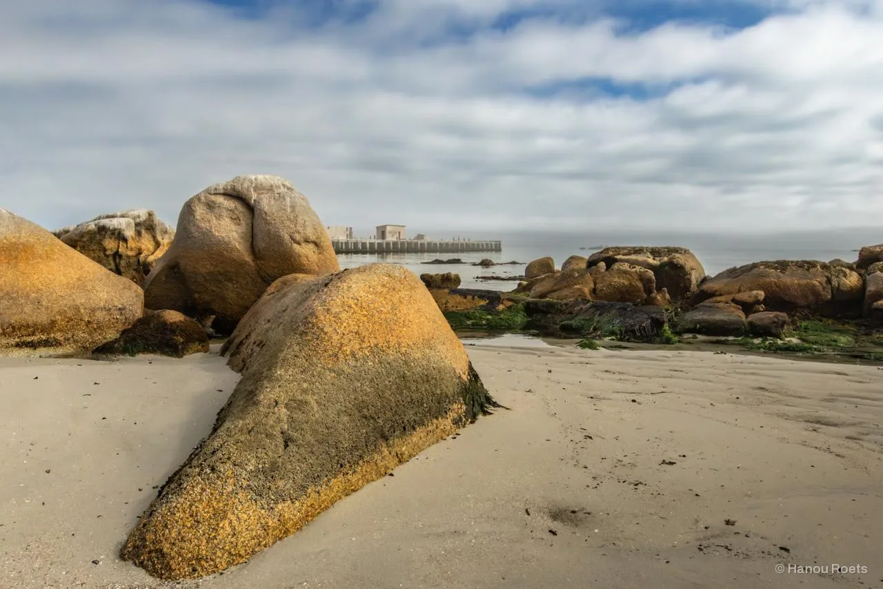 Orange lichen-covered granite boulders on a beach at low tide