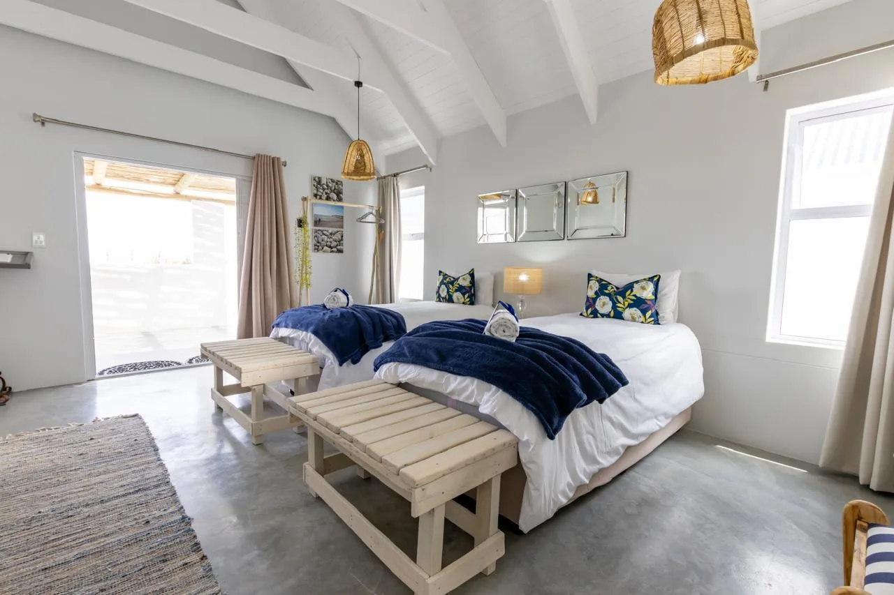 A bright guesthouse room with navy throws, white beams and a patio door