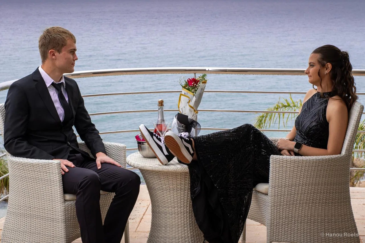 A matric couple sitting on a sea-view balcony, her sneakers up on the table