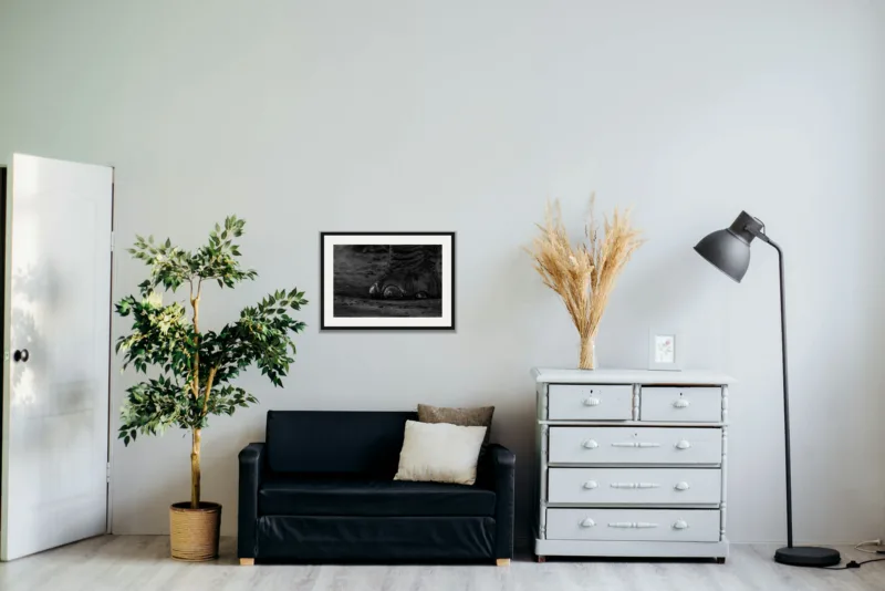 Footfall shown framed as an A2 print, above a black two-seater between a potted tree and a chest of drawers