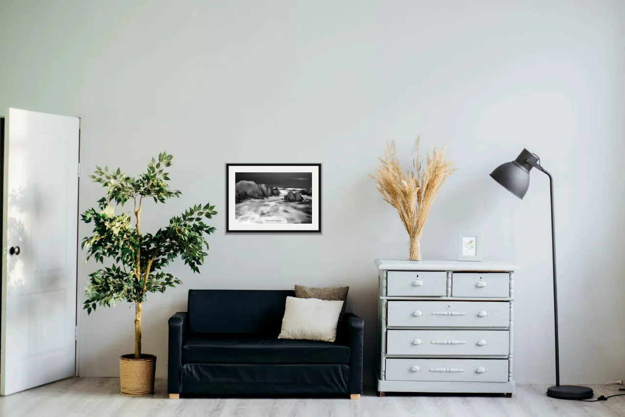 Granite and surf as a framed A2 print, above a black two-seater between a potted tree and a chest of drawers
