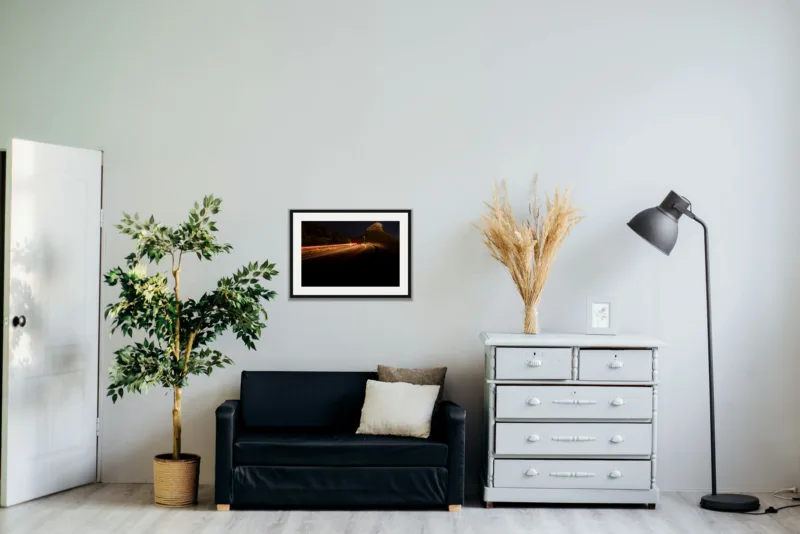 Night pass shown framed as an A2 print, above a black two-seater between a potted tree and a chest of drawers