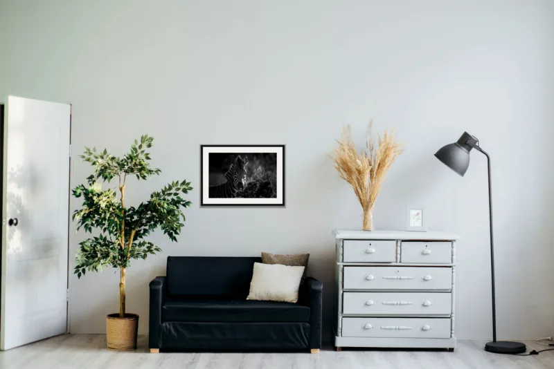 Backlit shown framed as an A2 print, above a black two-seater between a potted tree and a chest of drawers