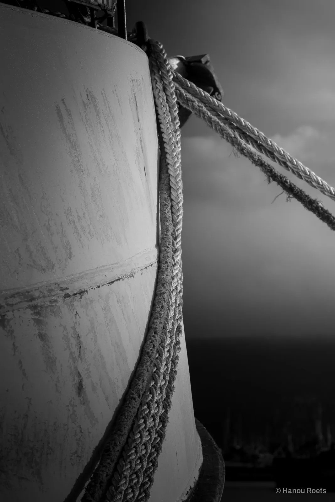Braided mooring ropes draped over the curved, weathered hull of a boat under a dark sky.