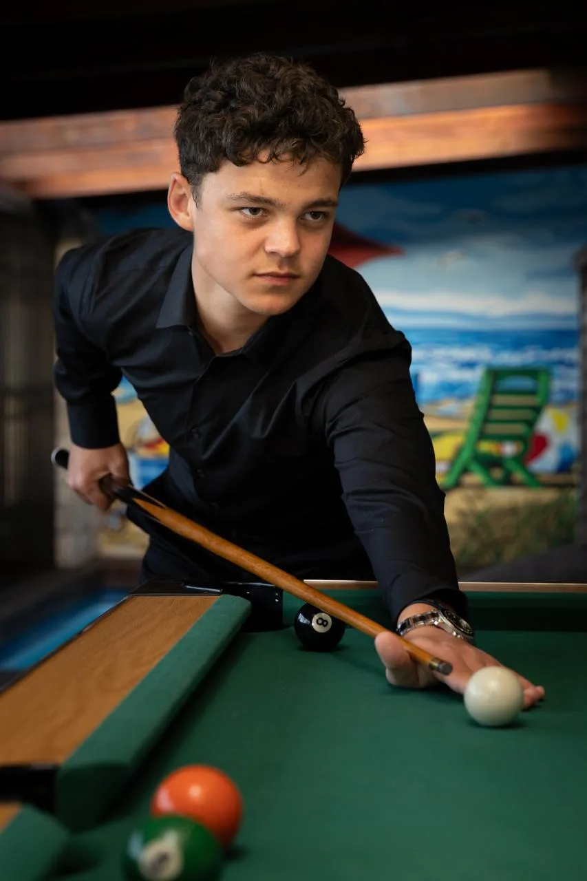 A young man in a black shirt lining up a shot at a pool table